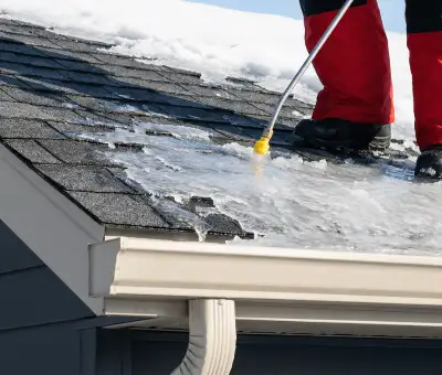 Ice dam removal technician using a steam wand to melt thick ice buildup on a residential roof in Little Rock, AR